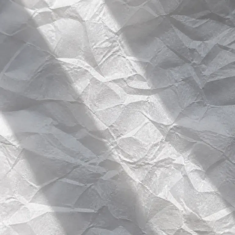 Close texture of crumpled translucent white paper with backlit folds and soft crossing shadows
