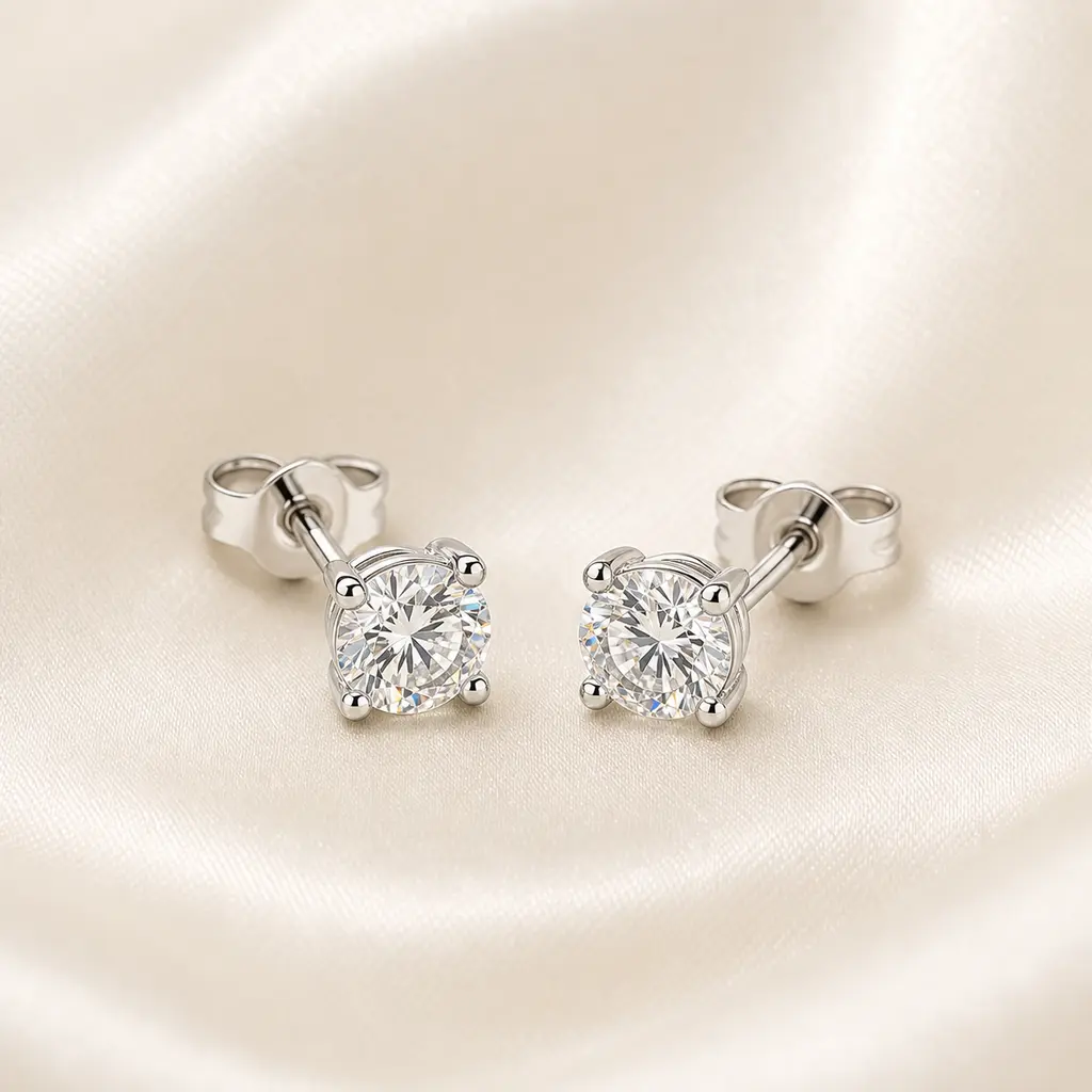 Pair of diamond stud earrings photographed at a 45-degree angle on crumpled ivory silk with brightfield lighting