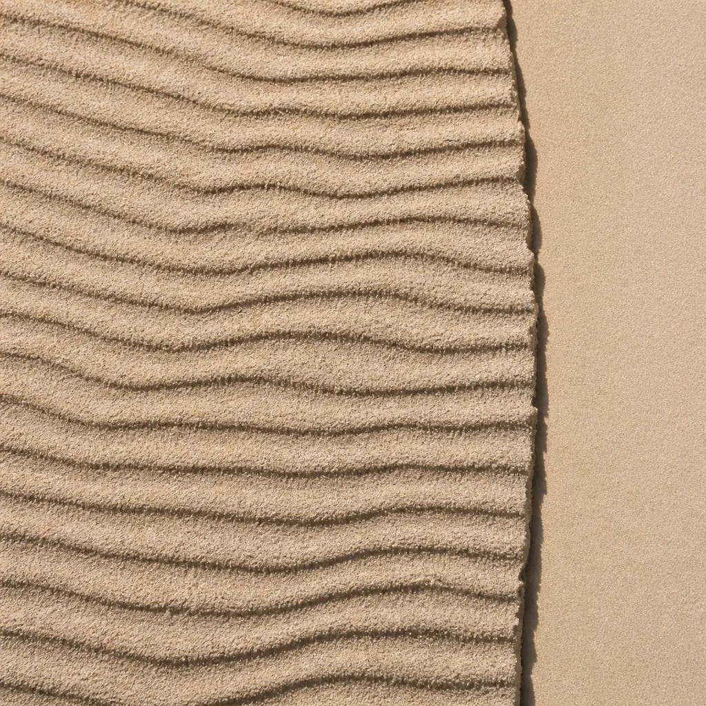 Fine pale sand with wind-made ripple ridges under hard raking sunlight