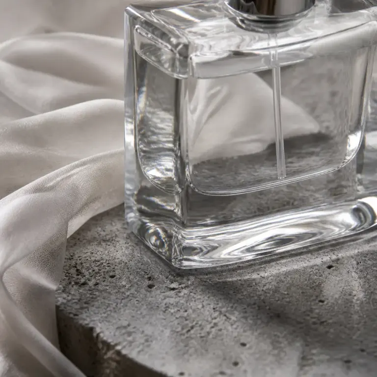 Extreme close-up of a clear perfume bottle refracting a rough stone slab beside draped translucent silk