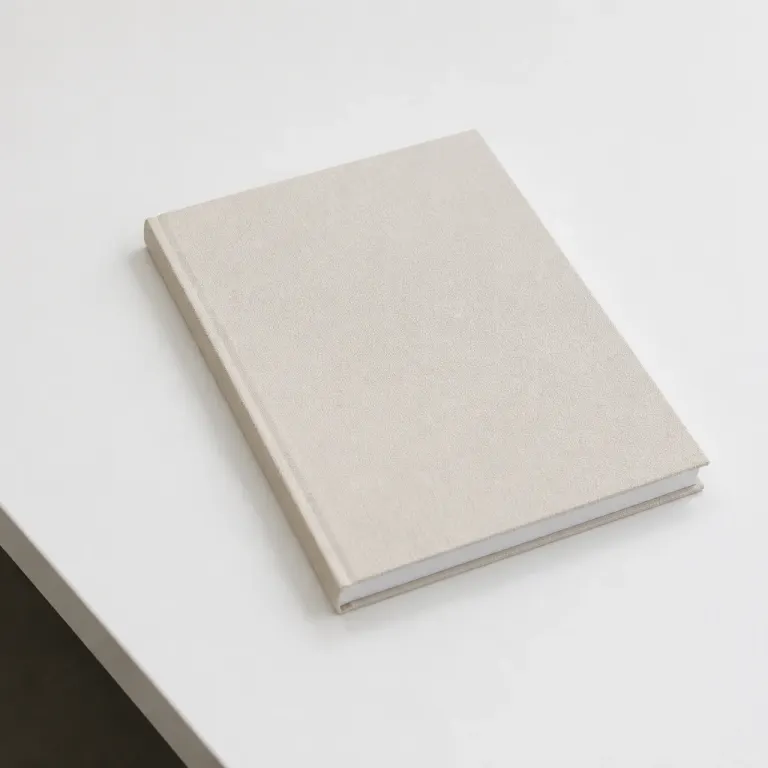 Closed clothbound notebook on a matte white desk in even overcast light