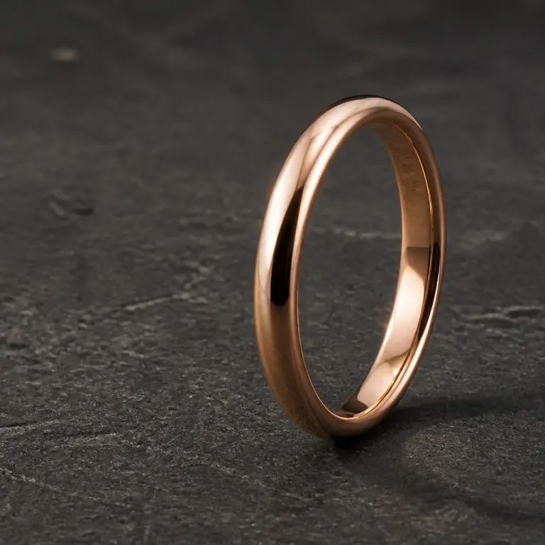 Polished rose-gold band standing on its edge on dark charcoal stone with raking side light