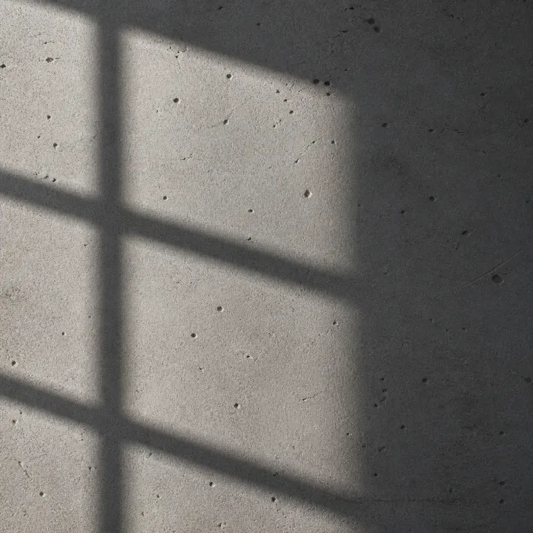 Rough grey concrete with fine pores and a geometric window shadow in side light