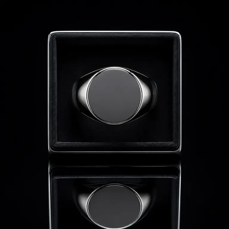 Top-down dark-field photograph of a blank black signet ring in a tray with a symmetrical mirror reflection