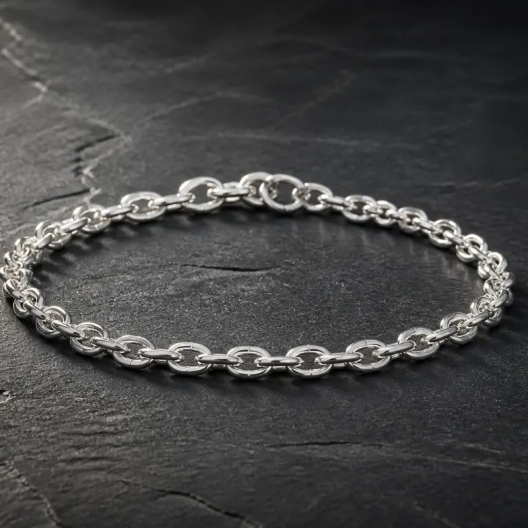 Fine silver chain bracelet coiled on dark charcoal stone with raking side light