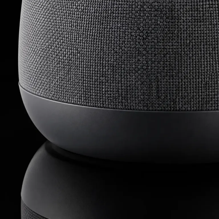 Extreme close-up of a gray fabric and matte black wireless speaker reflected in black acrylic